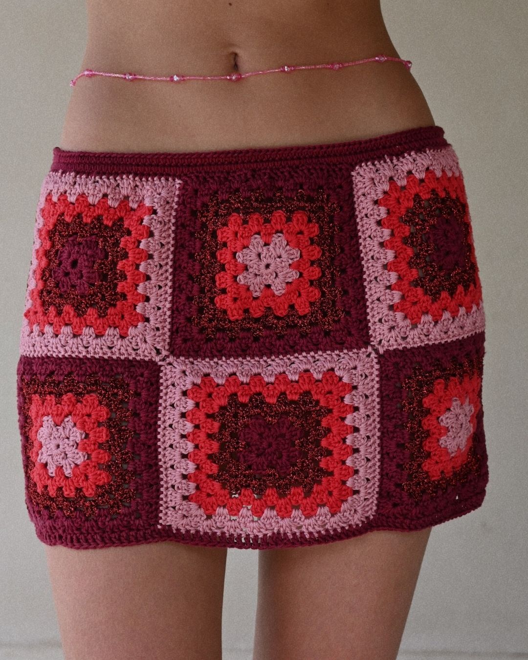 Extreme close-up of the Bianca skirt's crochet texture, showing the intricate red and fuchsia patterns and the quality of the hand-crafted weave.