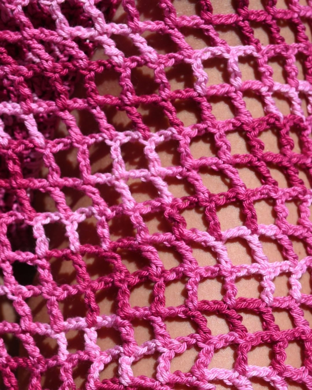 a close-up detail shot focusing on the open-network crochet weave of the fizz mini skirt. showing the gradient of vibrant magenta to light pink threads over the model's skin, highlighting the artisan texture.