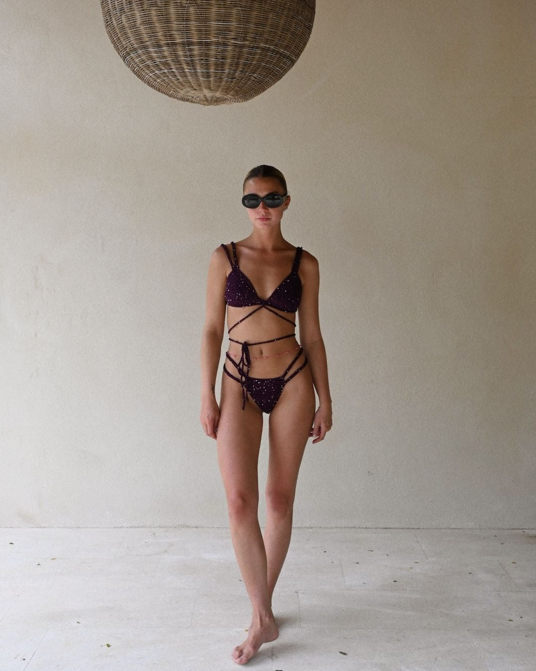 Full front view of a model standing indoors, wearing the vibrant deep plum Lila crochet bikini with large dark sunglasses.