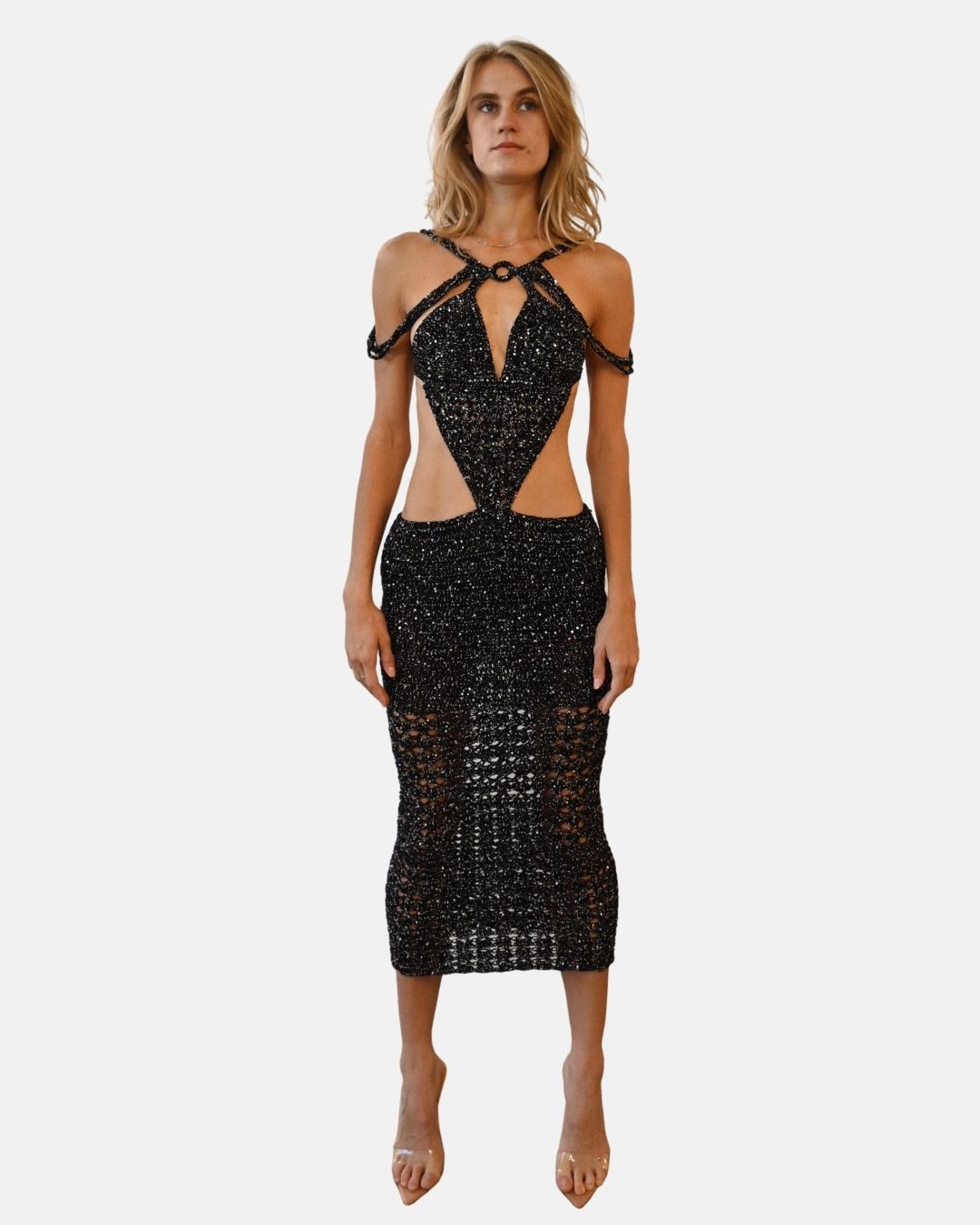 Full-length front view of a woman wearing the Melissa hand-crocheted maxi dress in black and silver. The dress features provocative waist cut-outs, a halter-style neckline, and shimmering sequin embellishments on an artisanal knit texture.