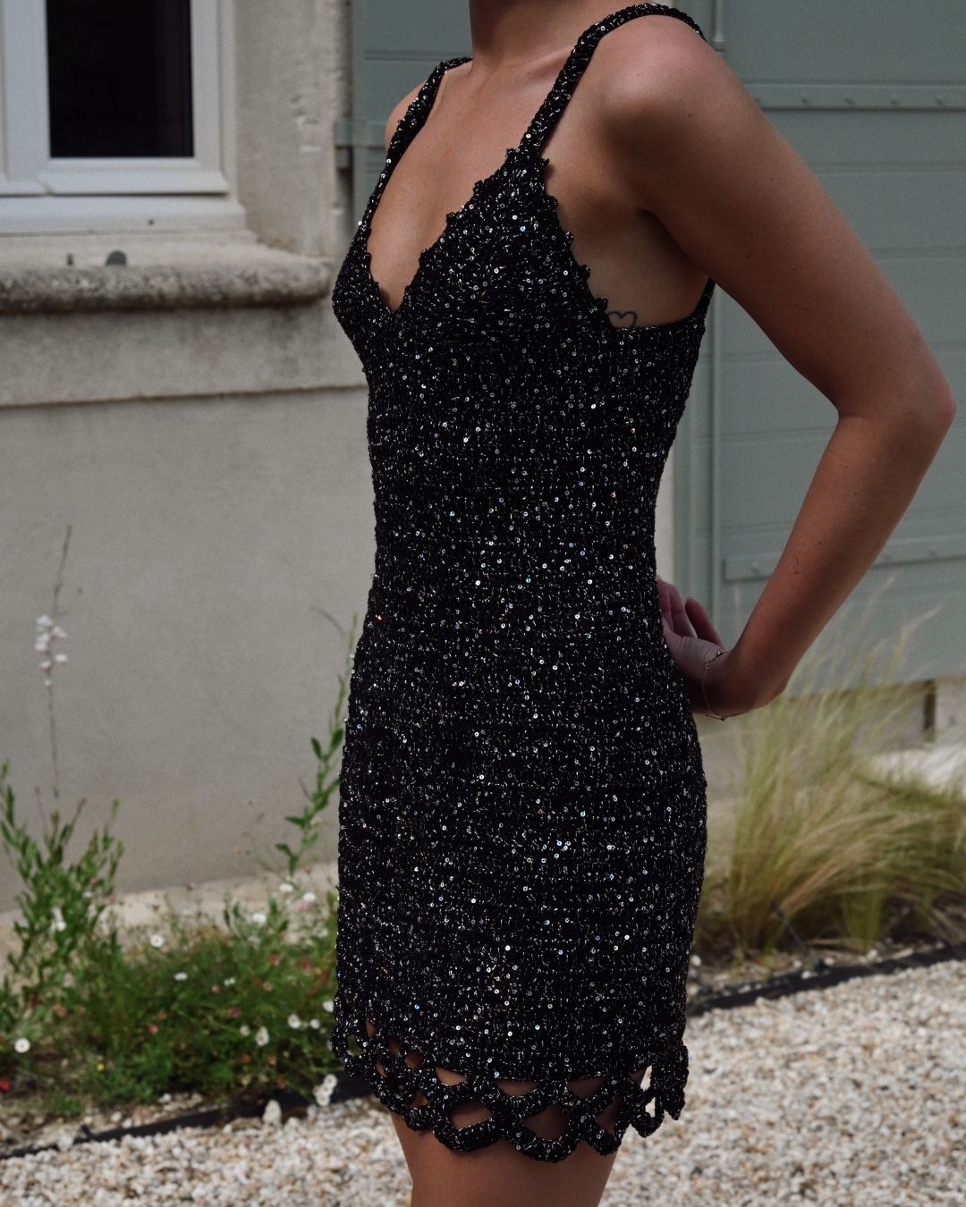 Side view of a model wearing the Apple Pie hand-crocheted mini dress, highlighting the delicate straps, the sequin-infused knit, and the scalloped hem detail.