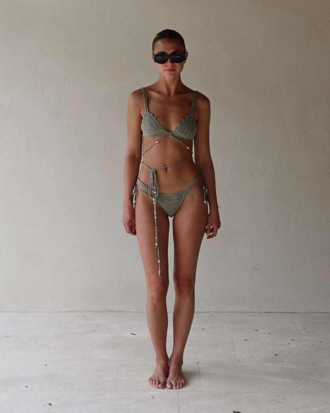 Front view of a model wearing the Sage Slate crochet bikini, highlighting the secure fit and the multicolor beads on the waist ties.