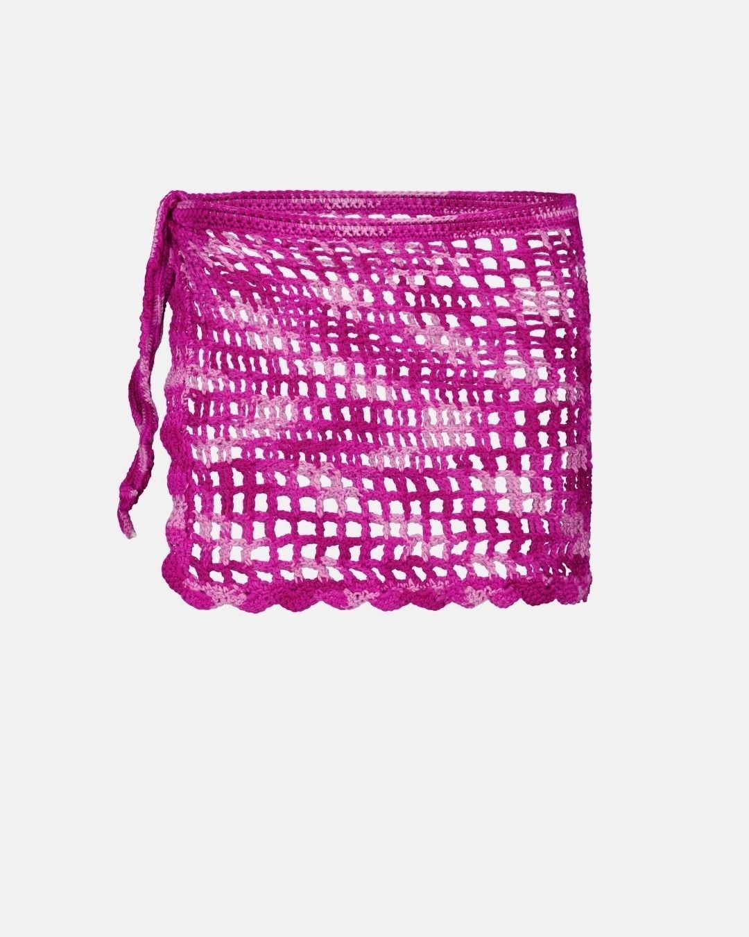 a flat lay packshot of the hand-crafted magenta and light pink open-knit crochet mini skirt from the sun-drenched collection. it features a side-tie and a scalloped hem on a neutral grey background.